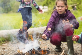 A child toasting marshmallows over an open camp fire at Colby Woodland Garden, Pembrokeshire.
